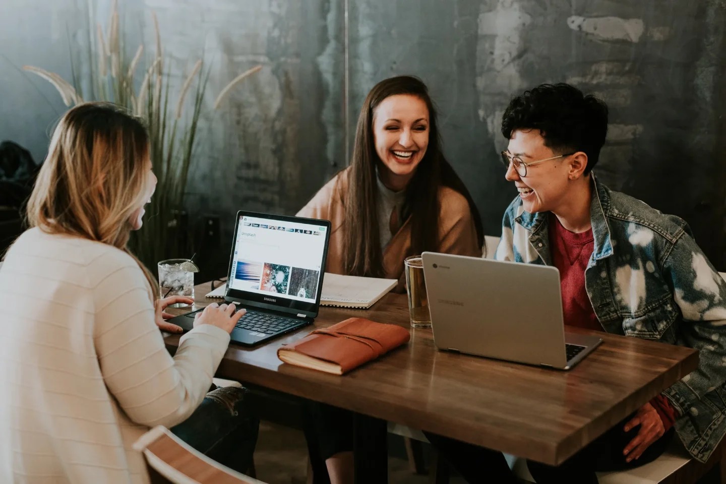 A group of three female colleagues working together on a laptop, engaged in a lively discussion about their technological tasks.